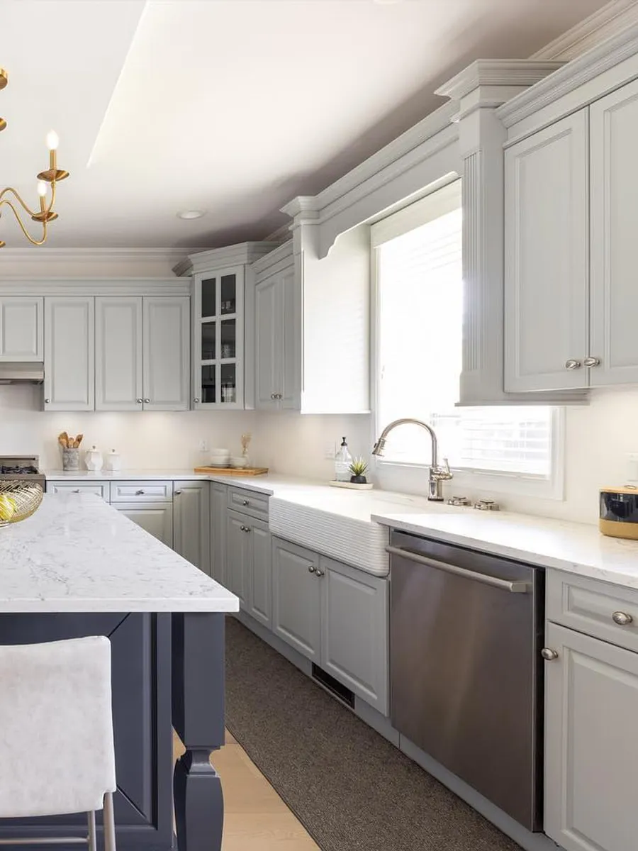 A finished kitchen with a marble-topped island, a farmhouse sink and a brass chandelier.