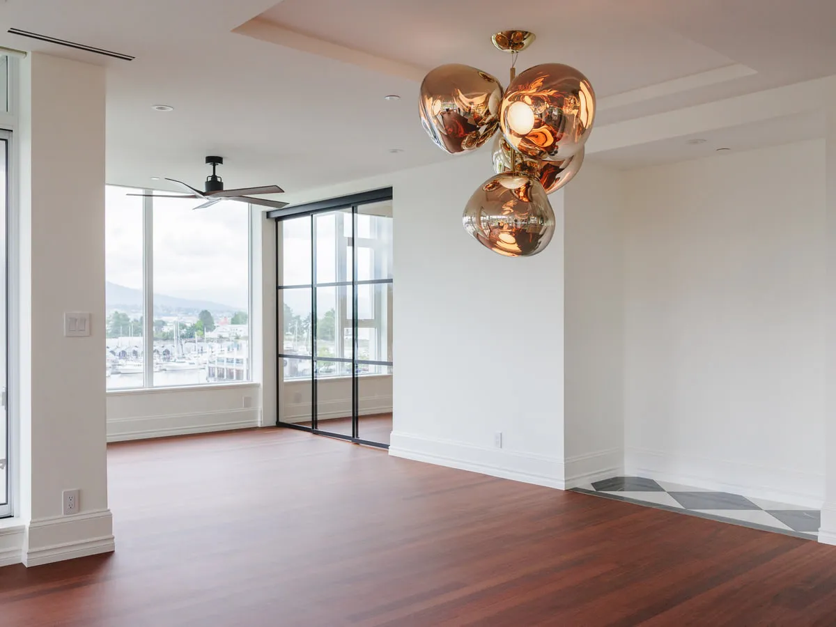 The finished open living area of a waterfront condominium, with a sculptural pendant cluster, refinished hardwood and the marina beyond the windows.