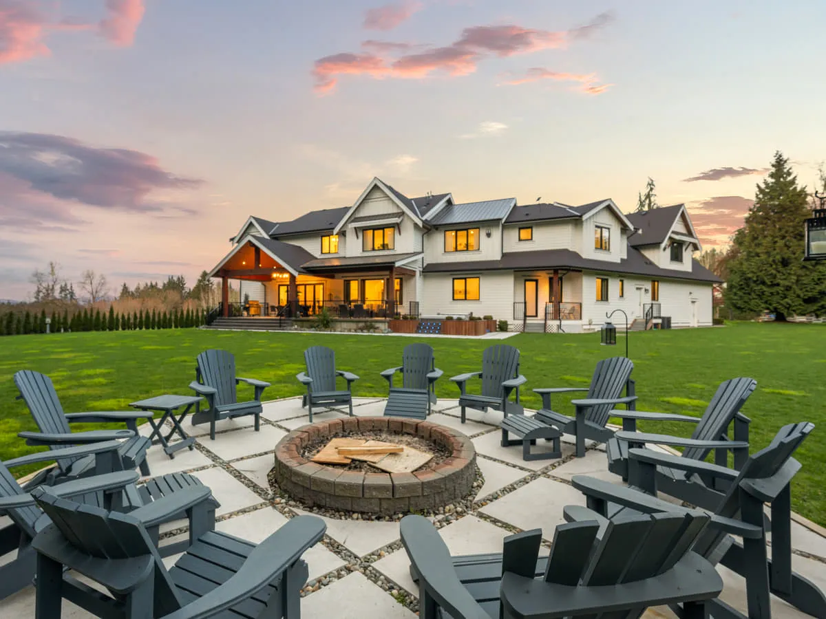 The rear elevation of a finished custom home at dusk, with a lawn, a fire pit and seating.